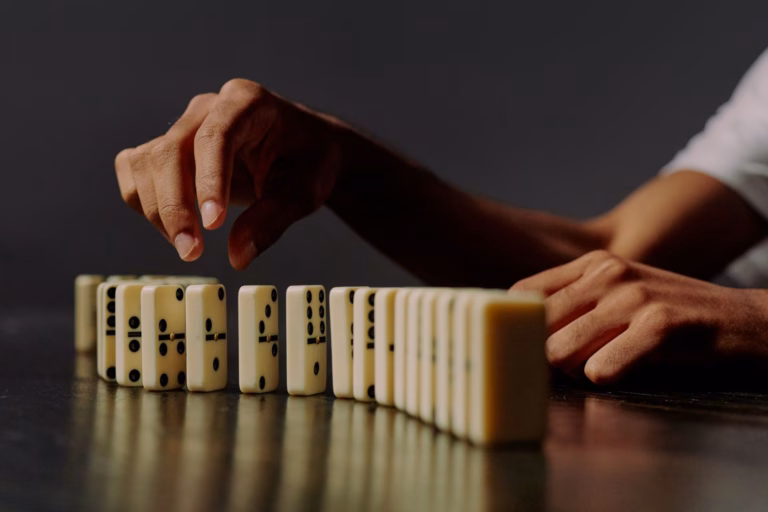 Une main s'apprête à faire tomber la première d'une rangée de dominos, symbole du sophisme de la pente glissante